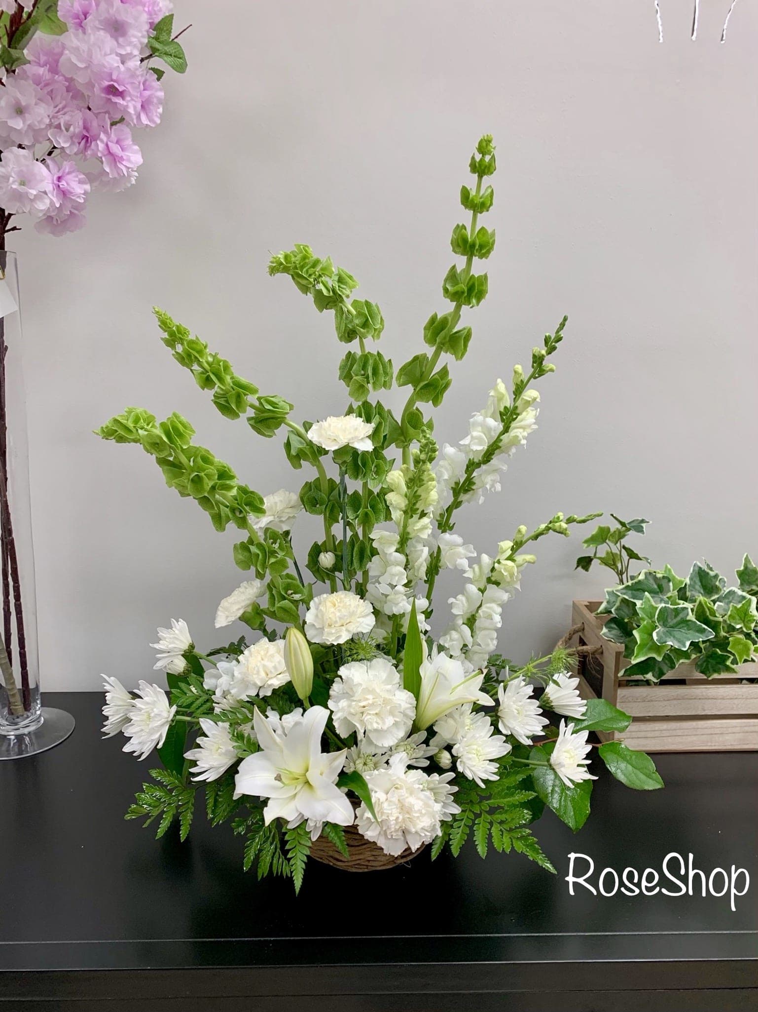 White lilies and daisies in a low basket arrangement with tall green spikes