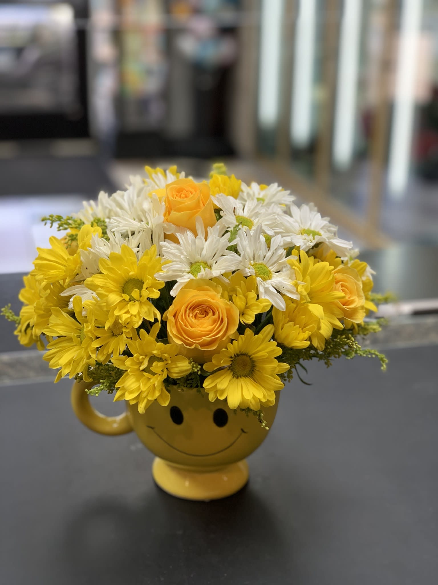 Yellow and white flowers arranged in a smiley-face mug