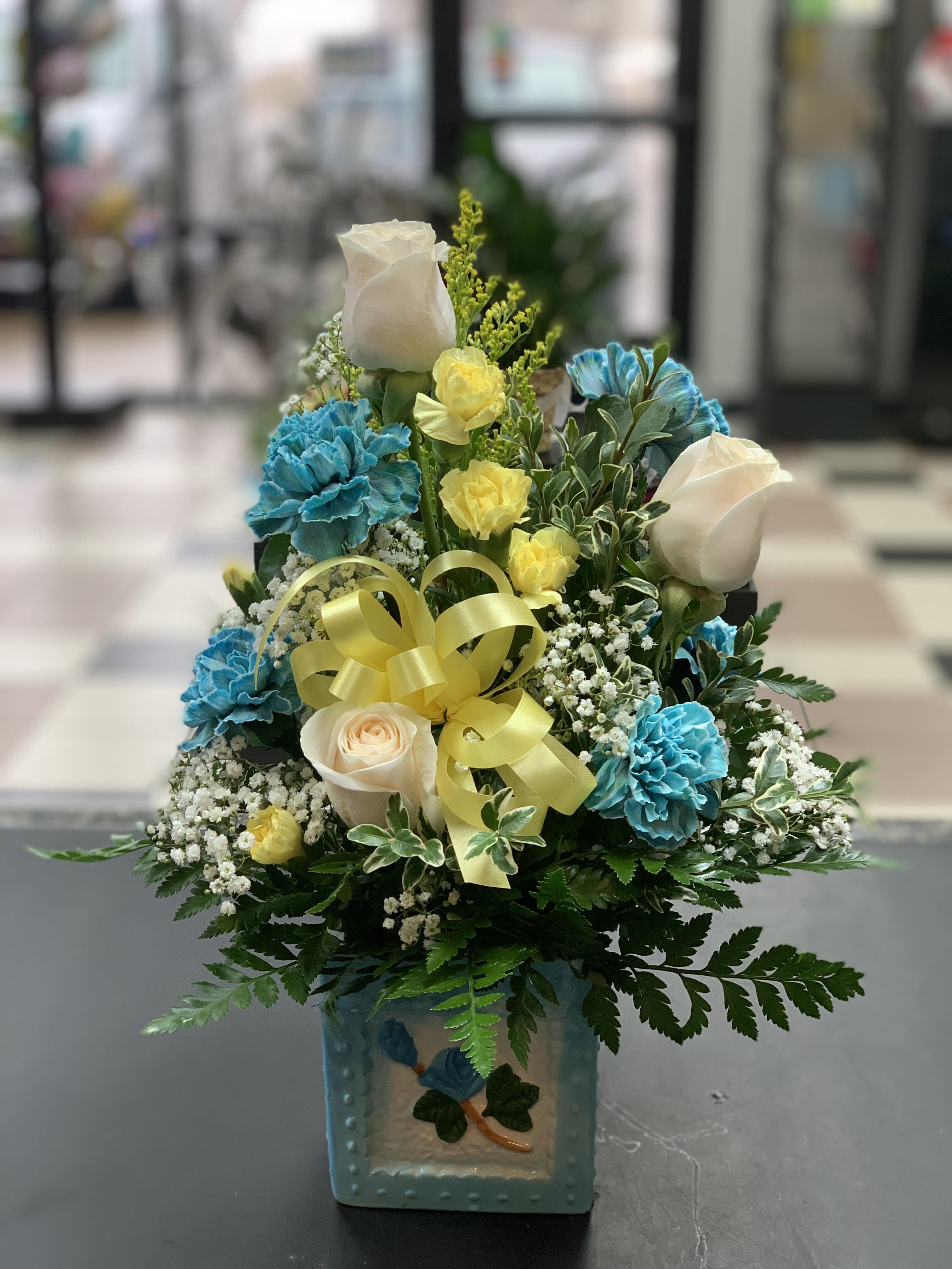 Blue and white floral arrangement in a decorative vase with a yellow ribbon