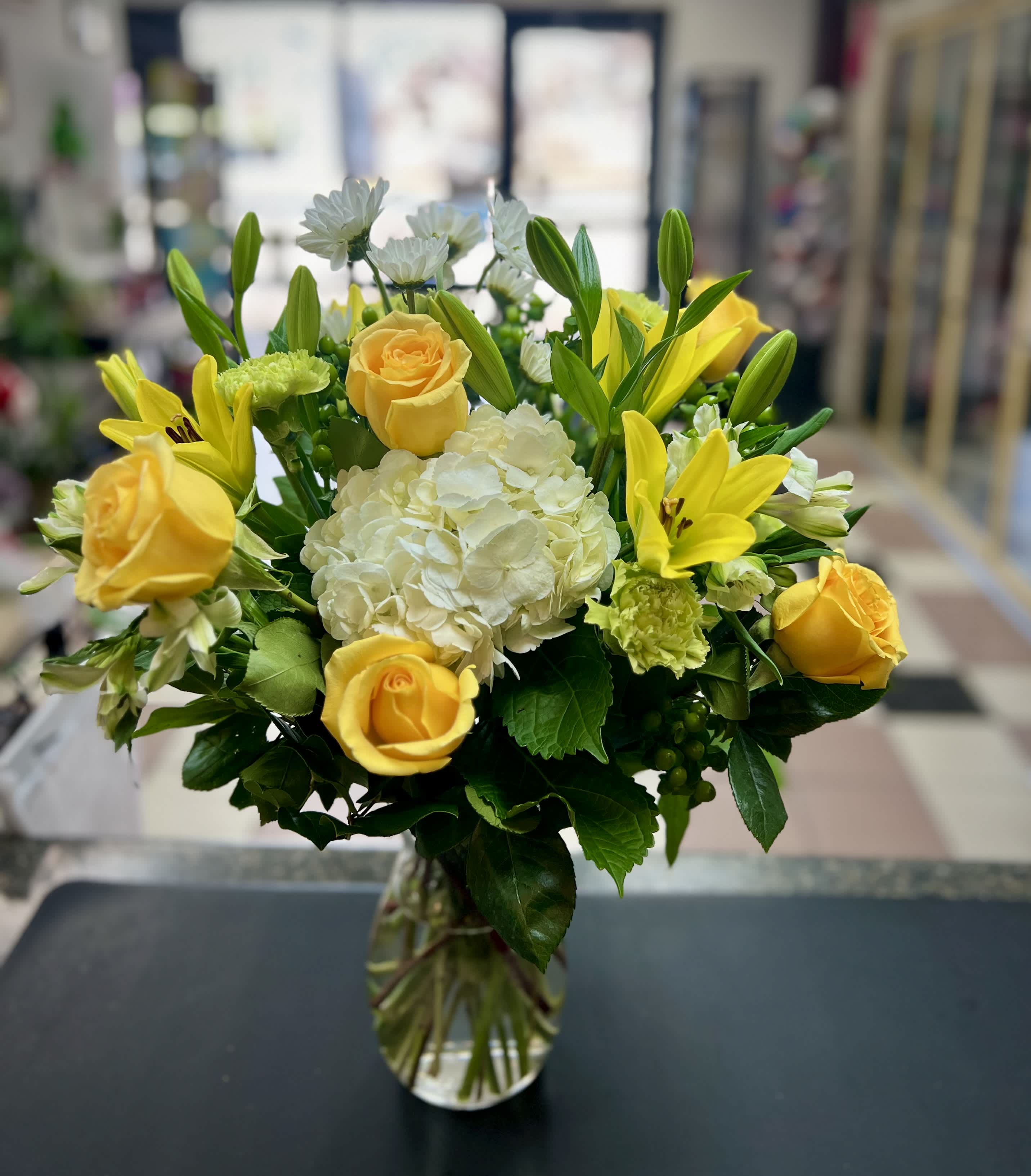 Yellow roses and lilies arranged with white hydrangea in a glass vase