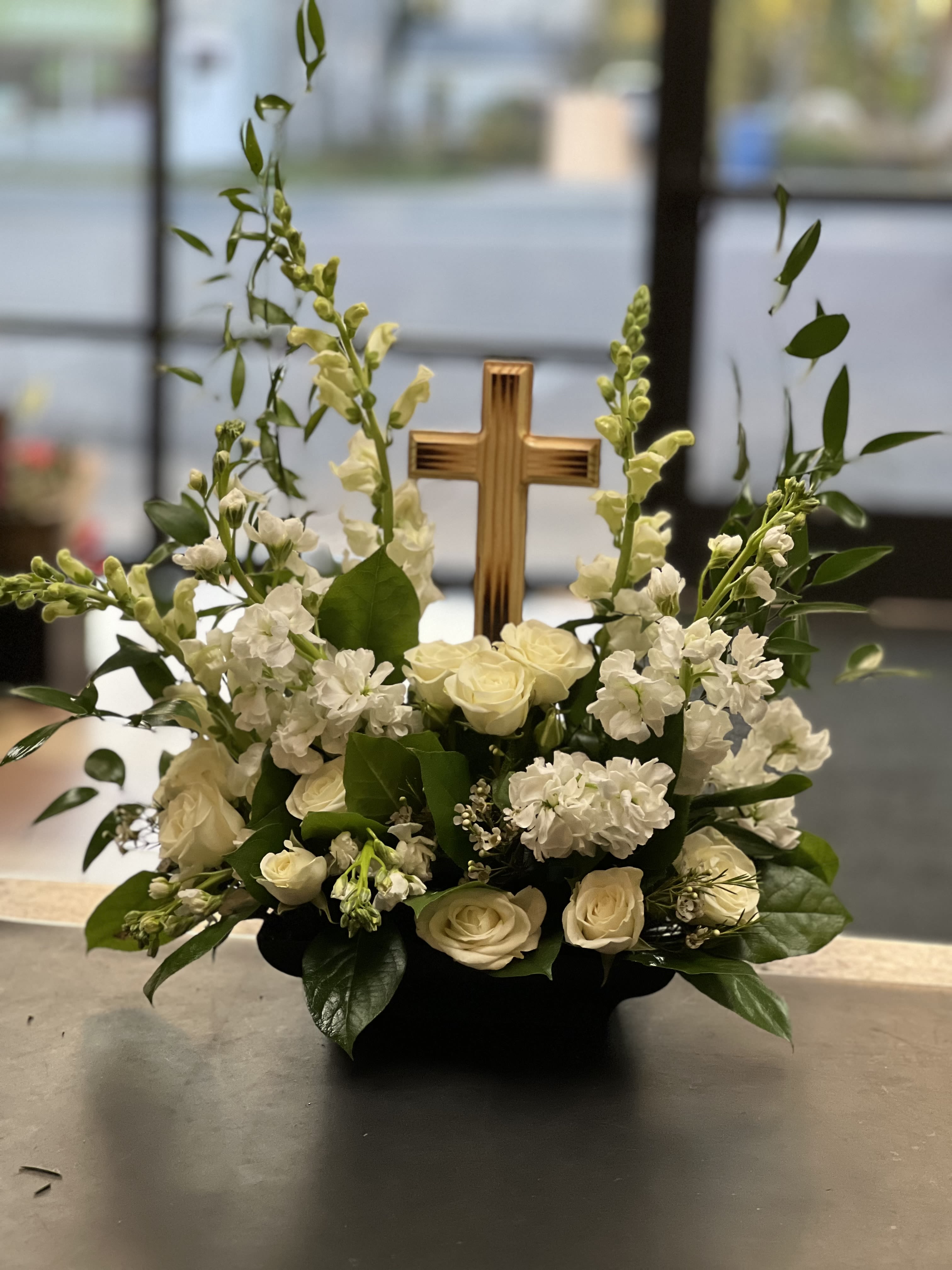 White roses and snapdragons arranged around a wooden cross