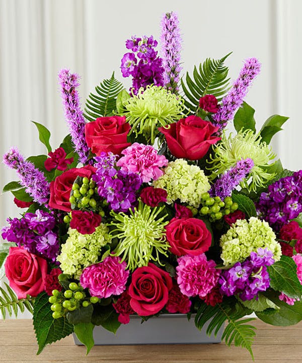 Mixed bouquet with red roses, purple blooms, and green flowers in a rectangular vase