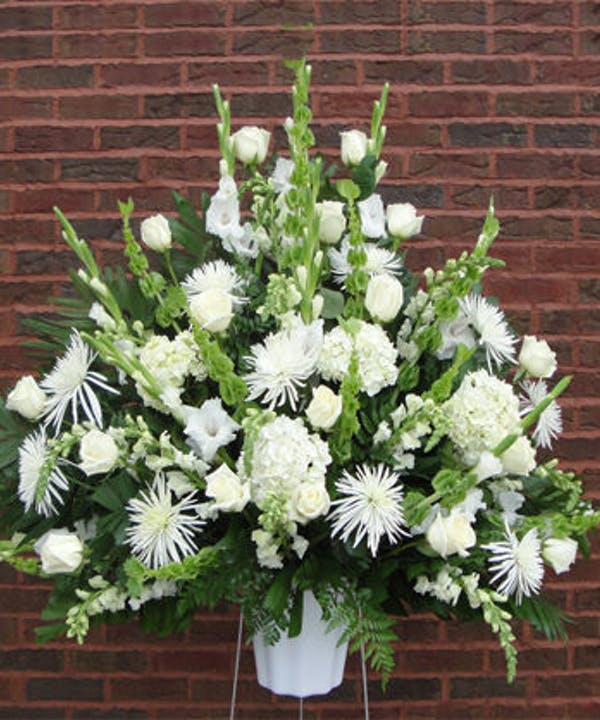 White floral funeral spray in a white container on a stand