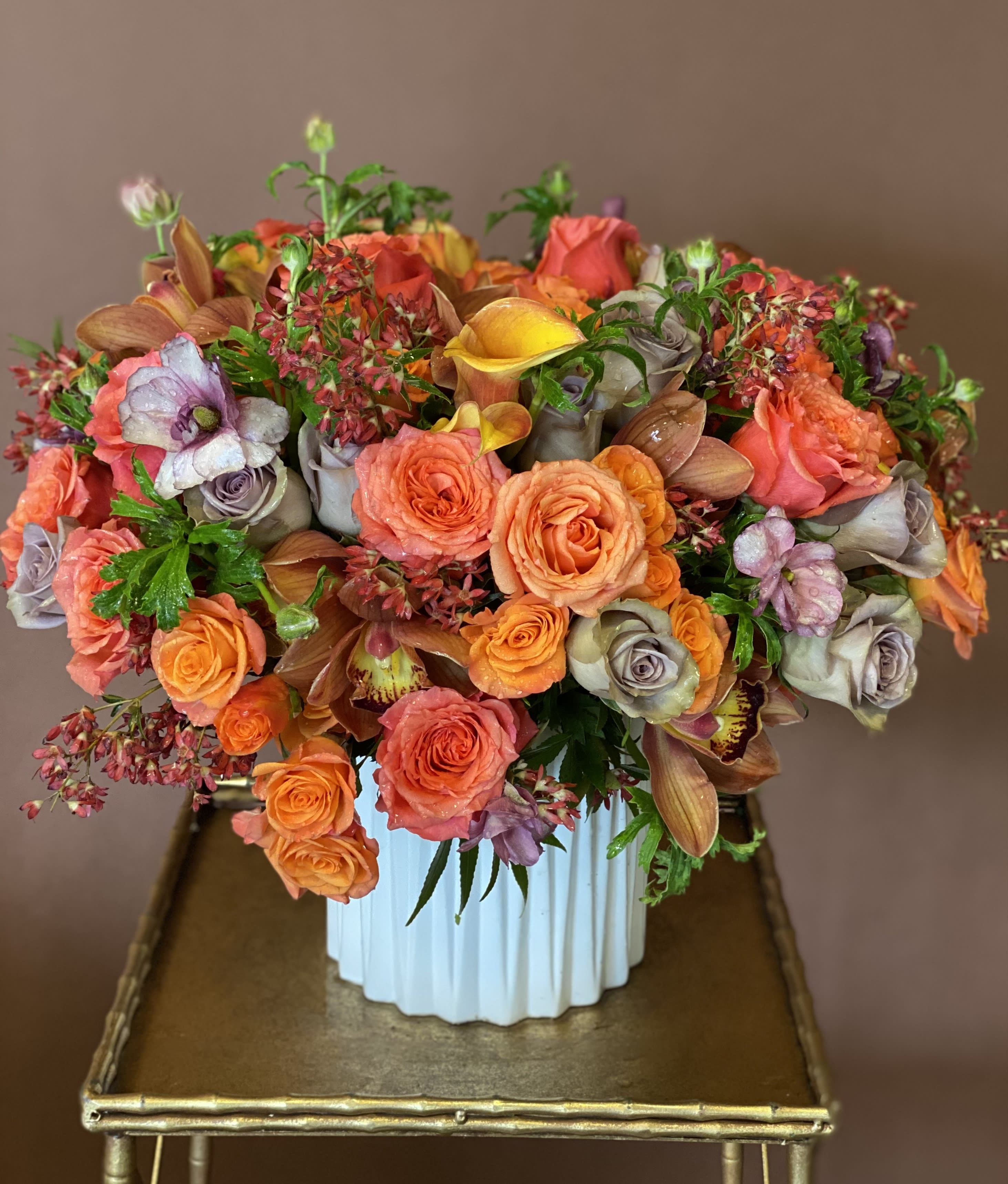 Mixed bouquet of orange, coral, and lavender flowers in a white vase