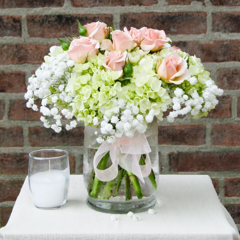Pink roses and white hydrangeas in a glass vase with a ribbon