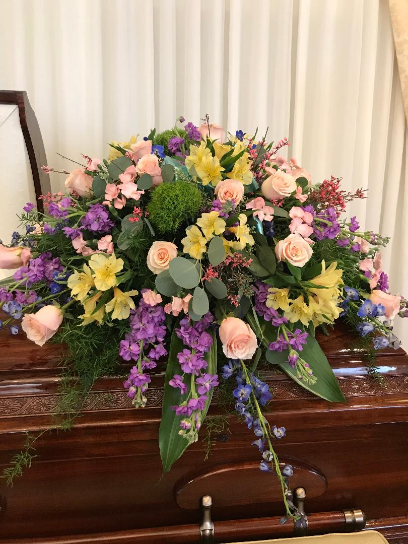 Large pastel floral spray on a wooden casket