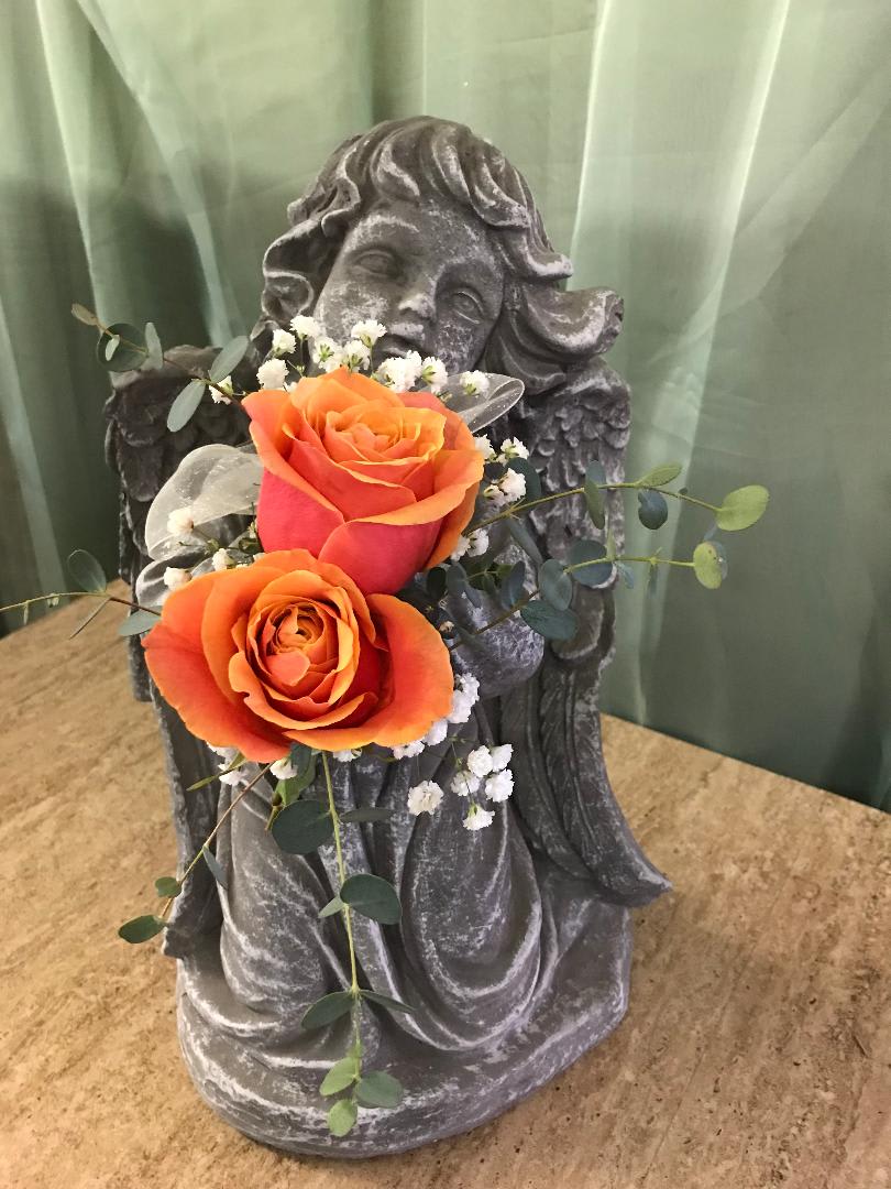 Two orange roses arranged on a stone angel statue
