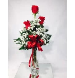 Red roses arranged with white baby's breath in a clear vase with a red ribbon