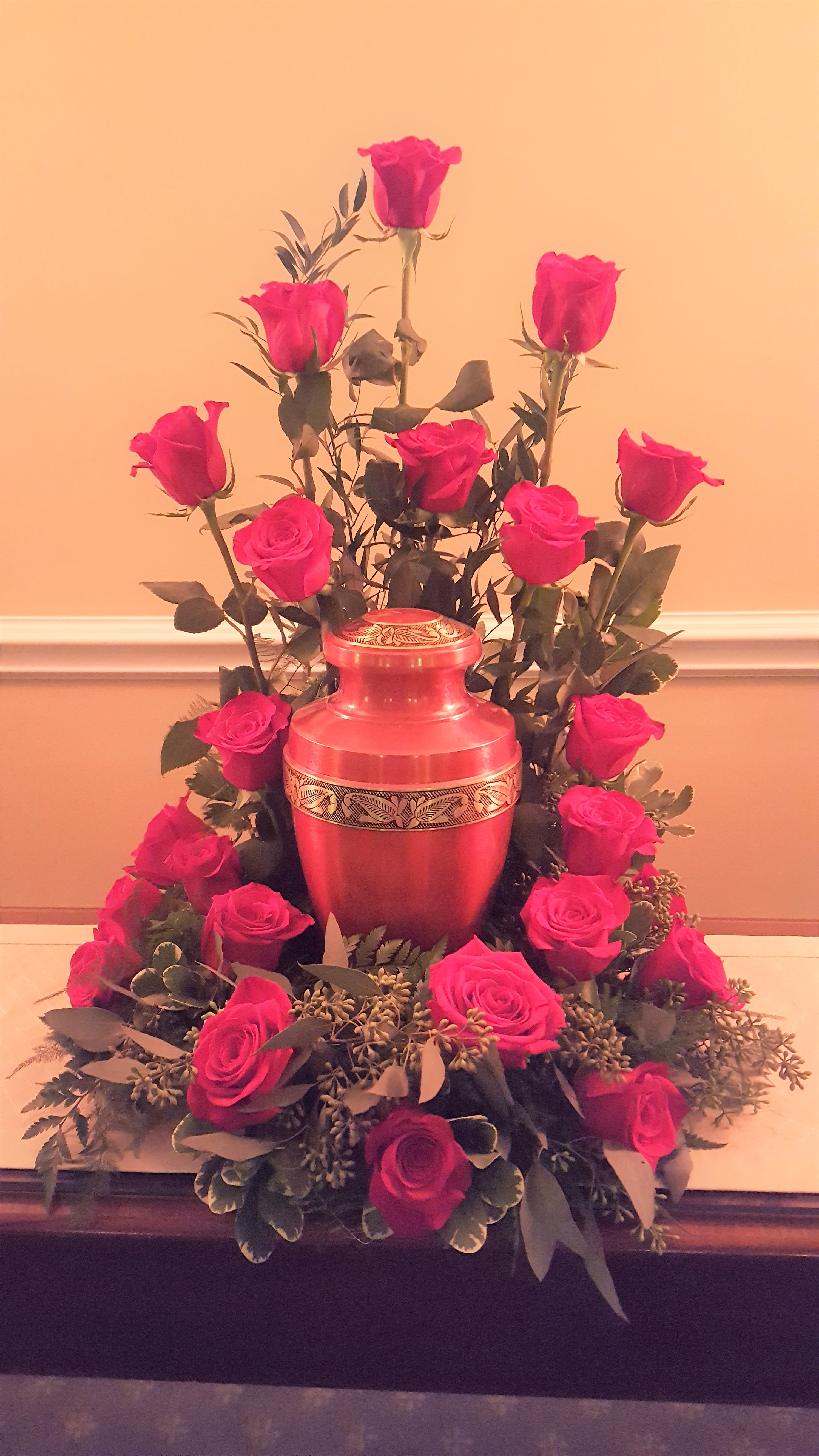Pink roses arranged around a red urn-shaped vase