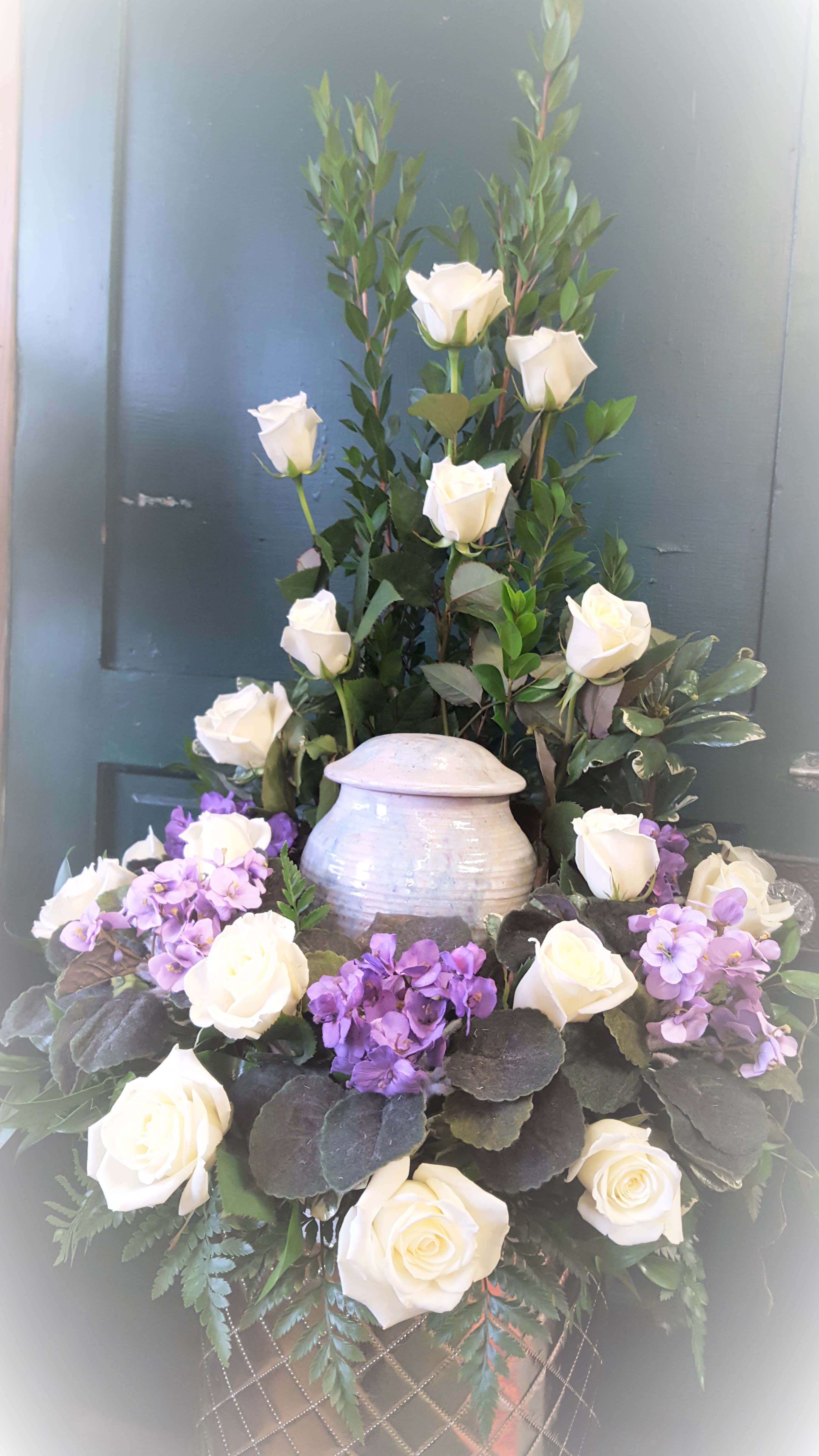 White roses and purple flowers arranged in a tall urn centerpiece