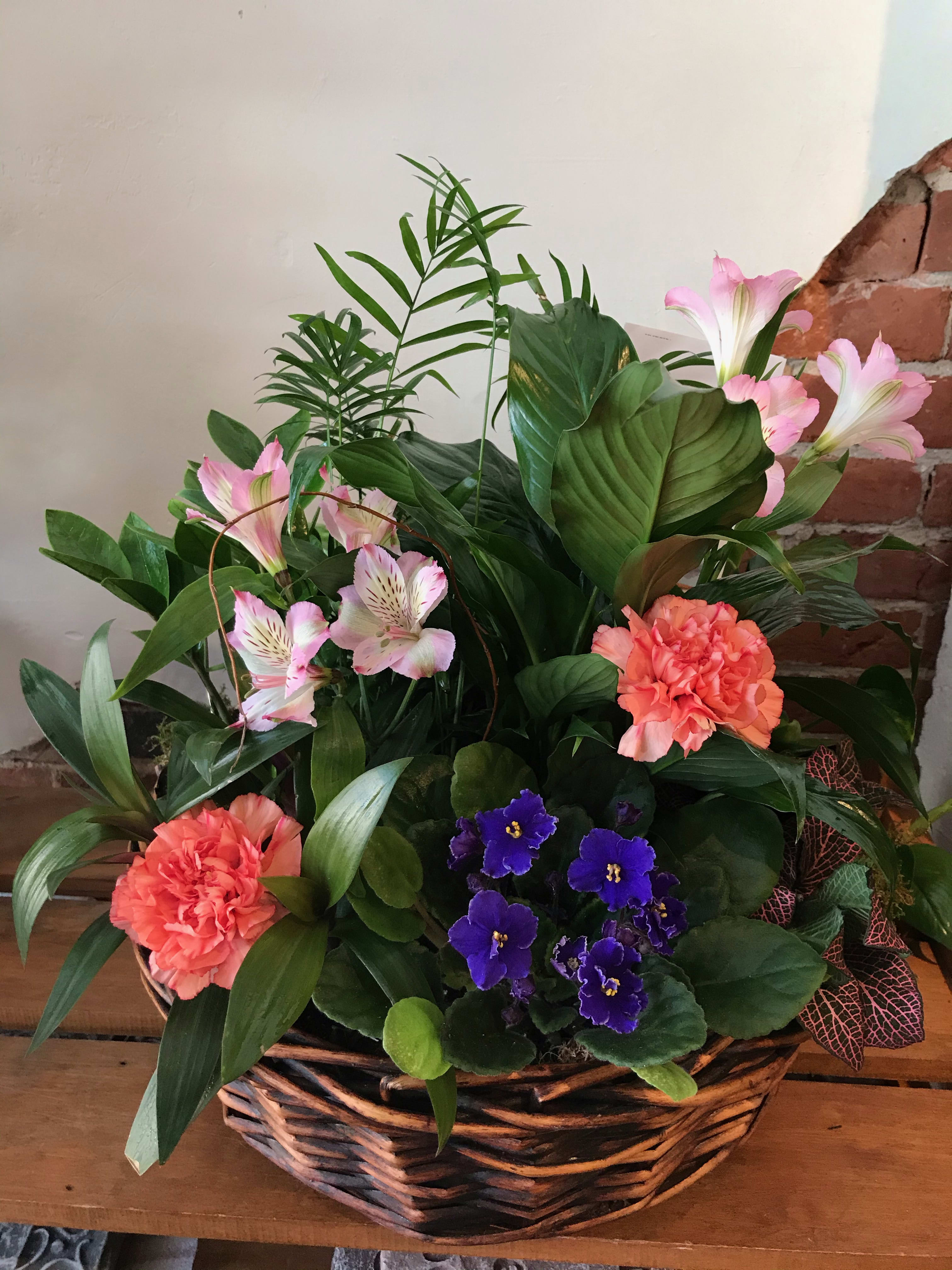 Basket arrangement with pink lilies, coral carnations, and purple violets
