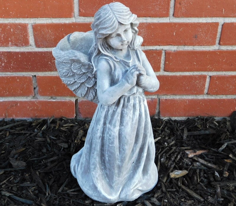 Gray angel statue standing against a brick wall