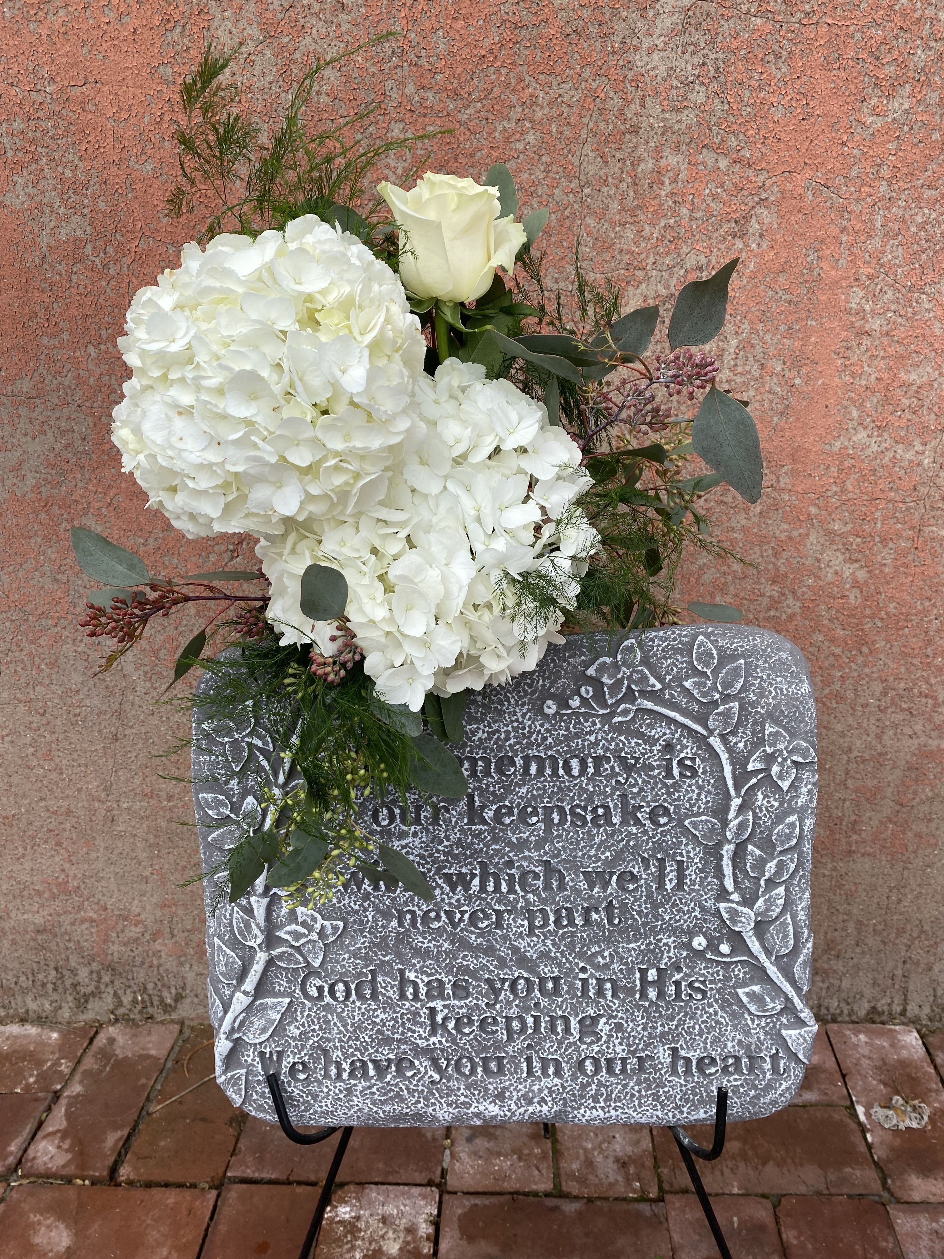 White floral spray on a memorial stone with a single white rose
