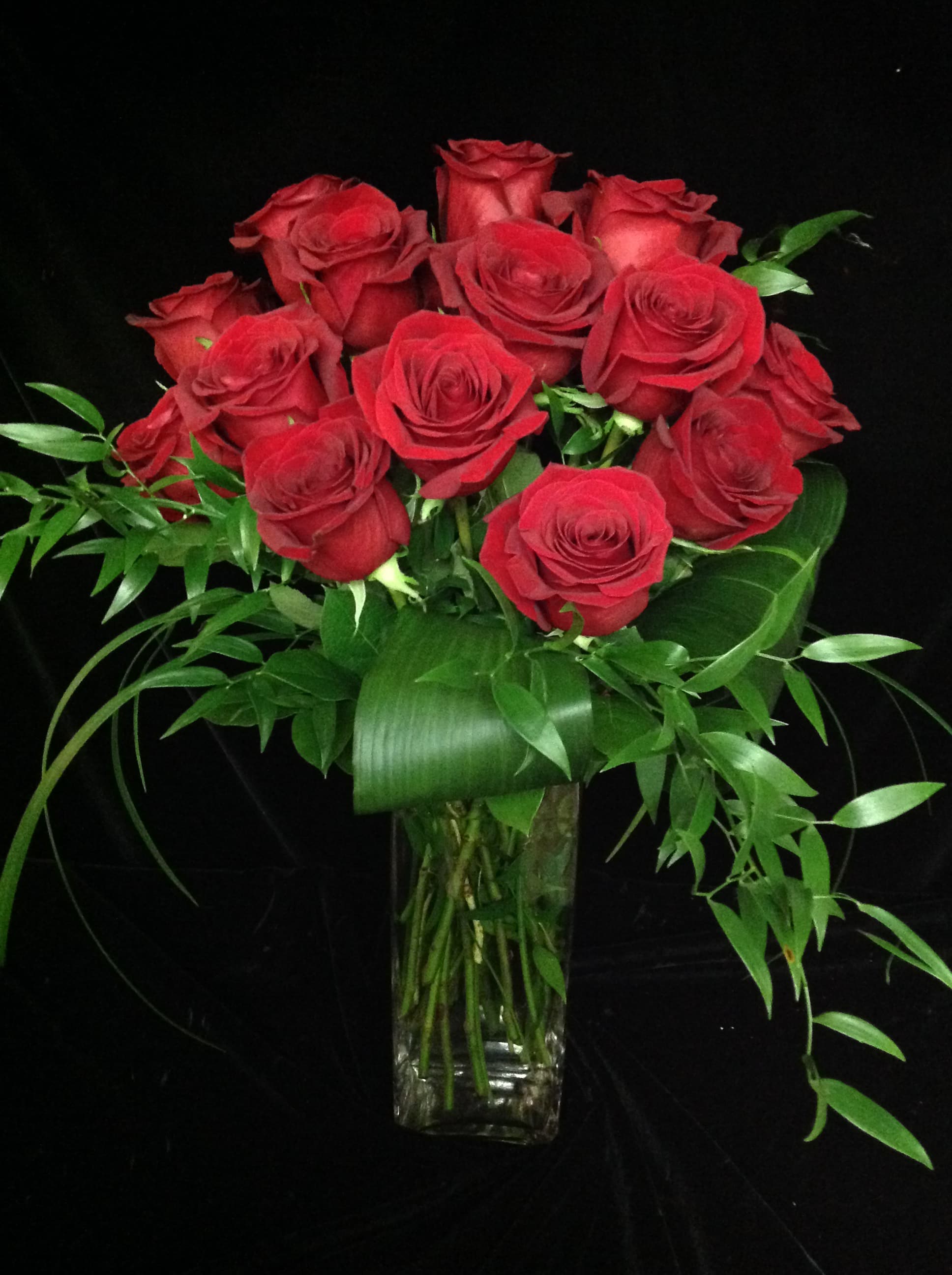 Tall arrangement of long-stemmed red roses with abundant foliage in a clear glass vase