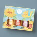 Sunflower-patterned gift box holding three small colored bottles on a gray surface