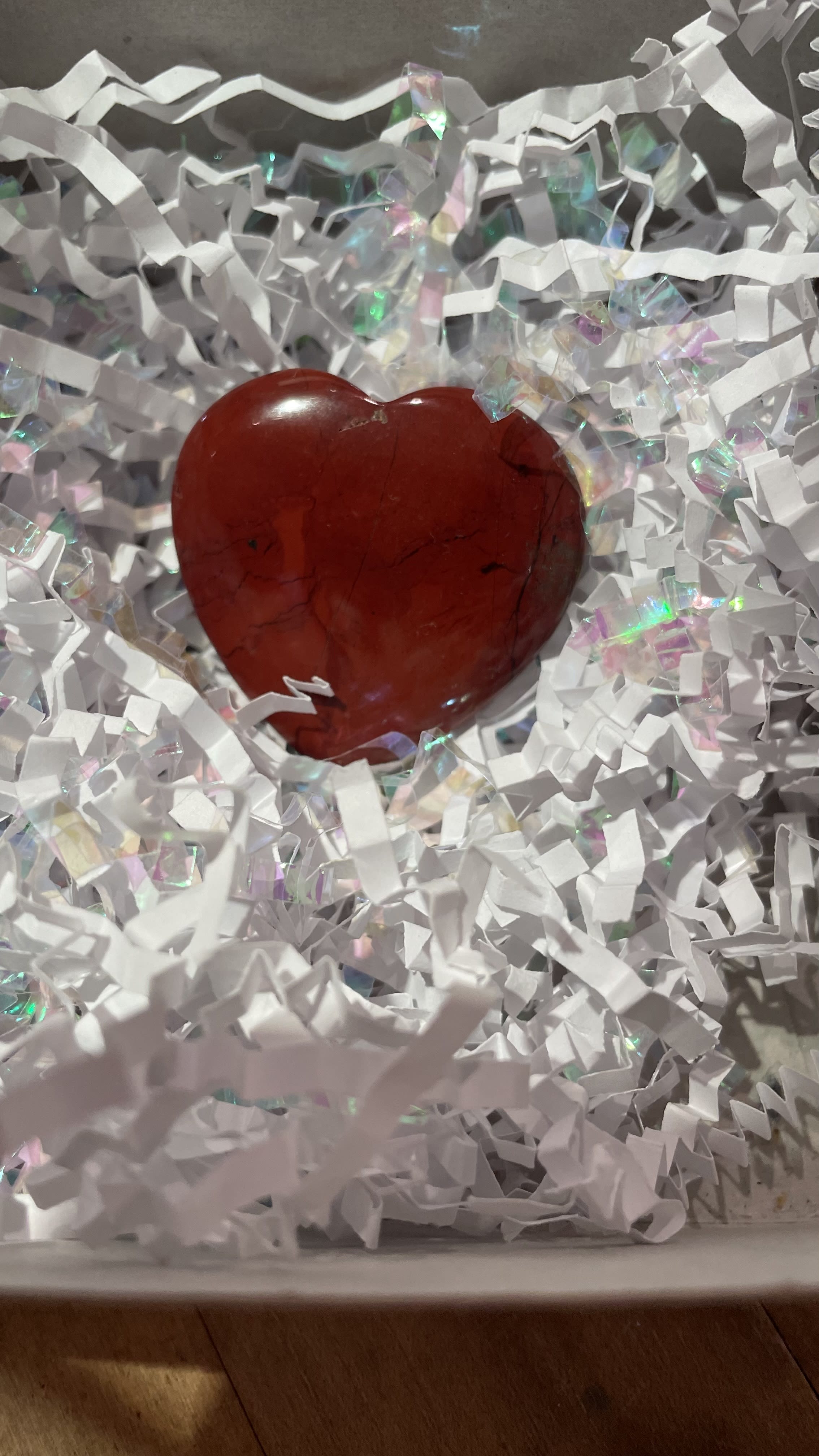 Red polished heart-shaped stone nestled in white crinkle paper filling