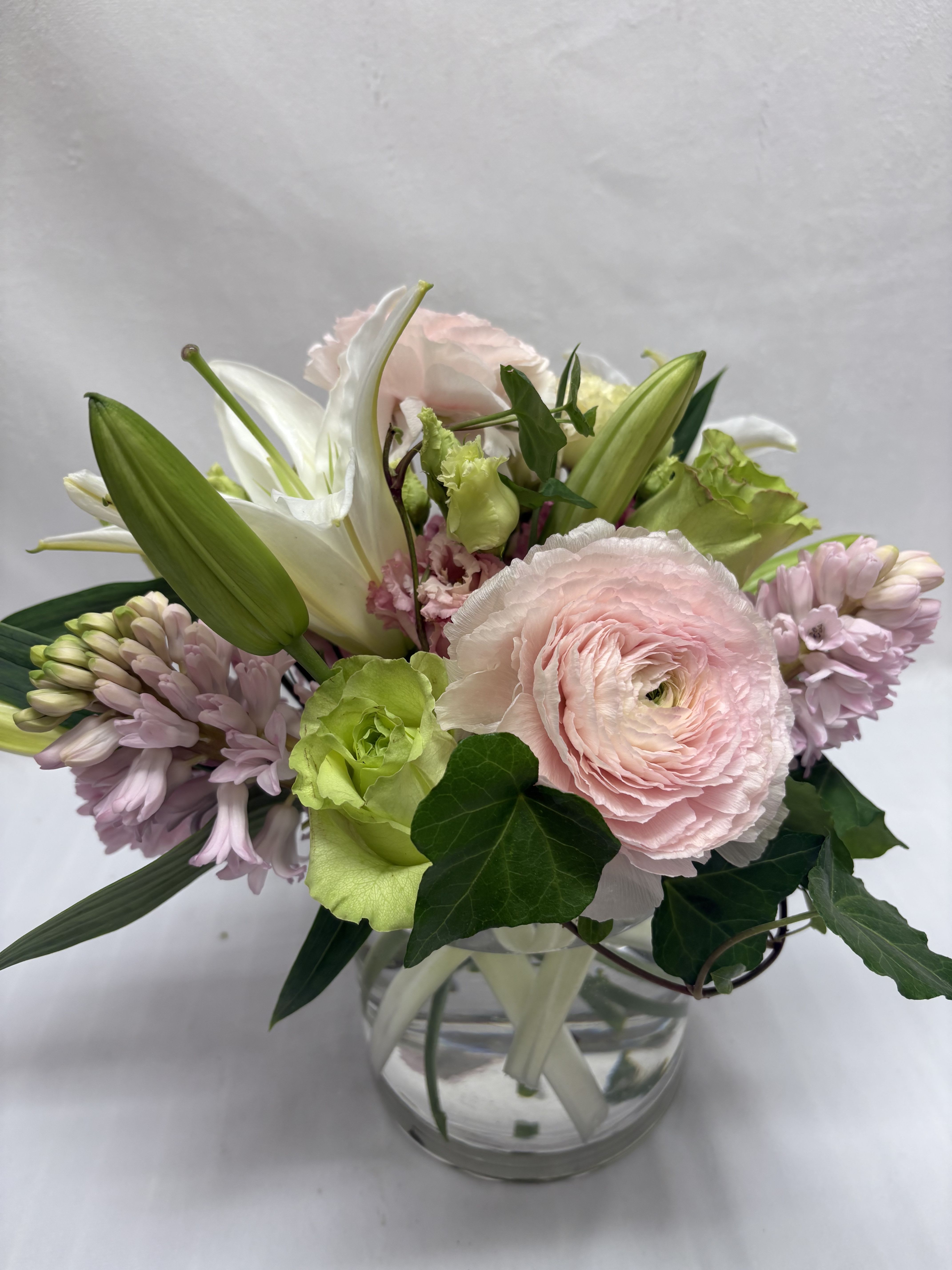 Pastel bouquet of pink ranunculus, lilies, and hyacinths in a round glass vase