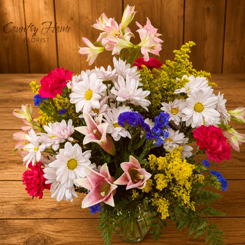 Mixed bouquet of daisies, lilies, carnations, and yellow filler in a glass vase