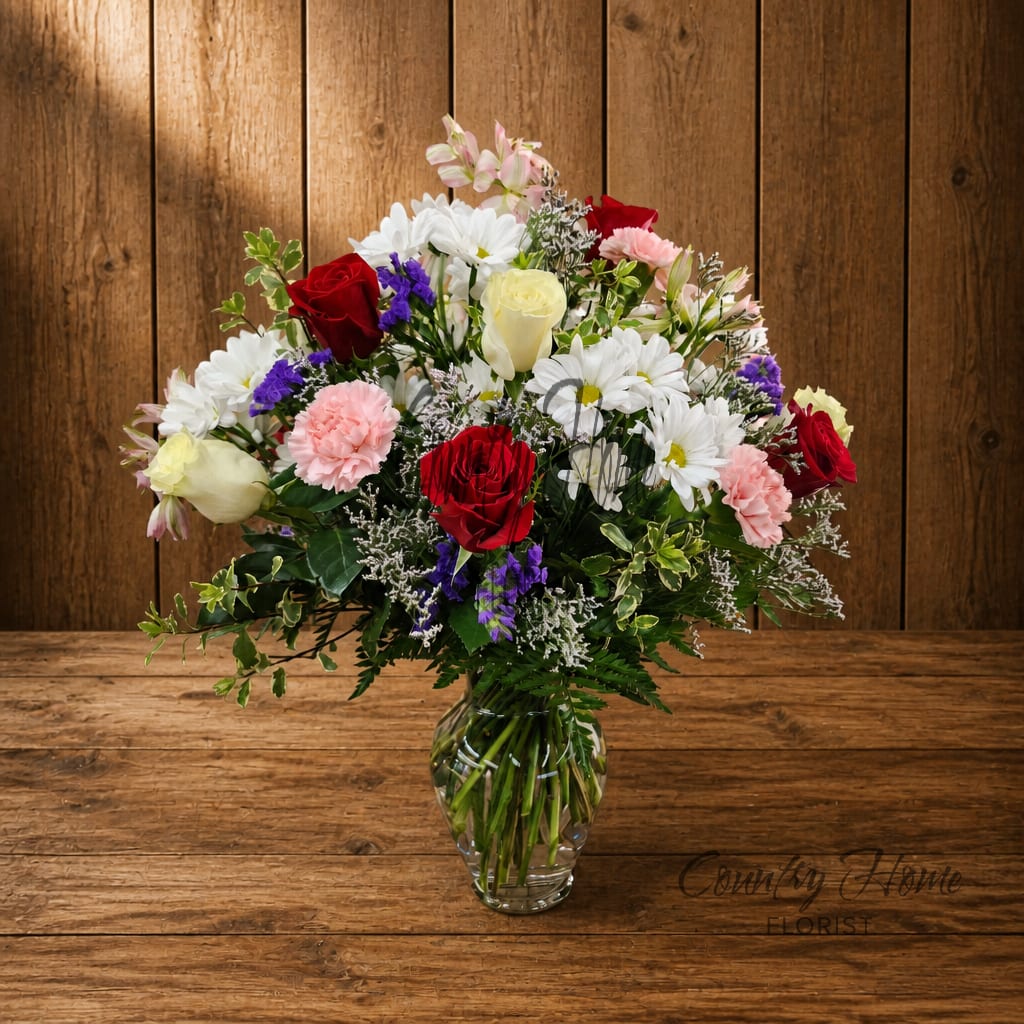 Mixed bouquet of roses, daisies, and carnations in a clear glass vase