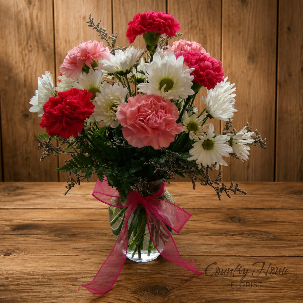 Pink and white carnations with daisies in a glass vase tied with a pink ribbon