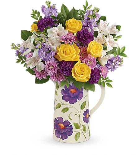 Bouquet of yellow roses, purple flowers, and white lilies in a floral pitcher vase
