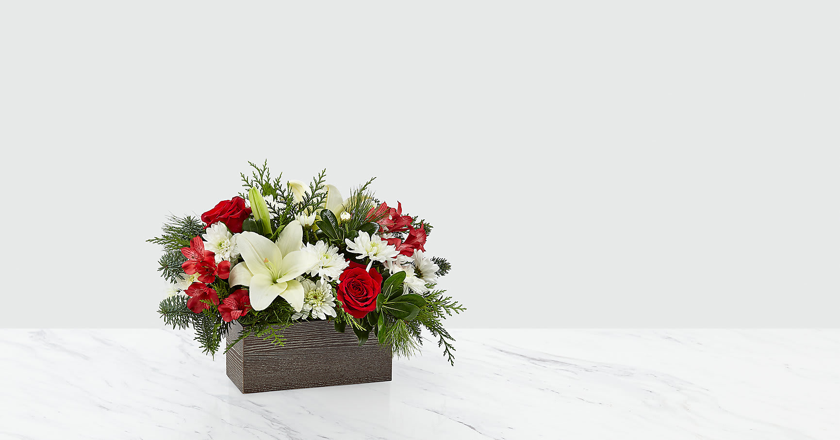 I'll Be Home™ Bouquet - Nothing says happiness and joy more like coming home to the ones you love most. An artful collection of white cushion pompons and Asiatic lilies with contrasting red roses and alstroemeria makes those precious moments this season all the more special. They all arrive in a rustic, weathered wooden rectangular box.  ITEM #18-C15S
