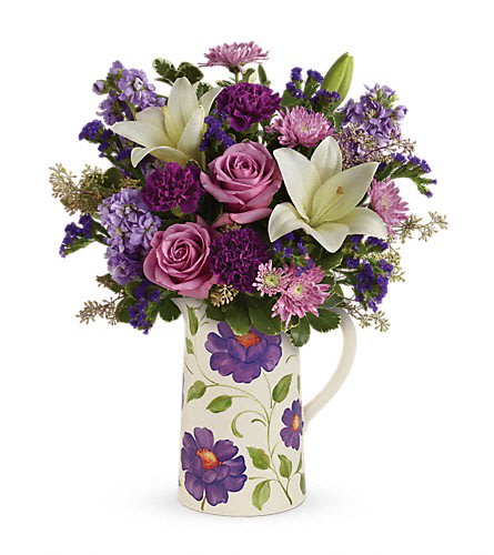 Purple and pink bouquet with white lilies in a floral pitcher vase