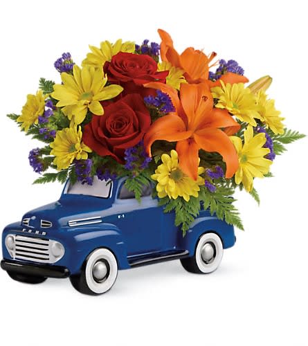 Flower arrangement in a blue toy truck with red roses, orange lilies, and yellow daisies
