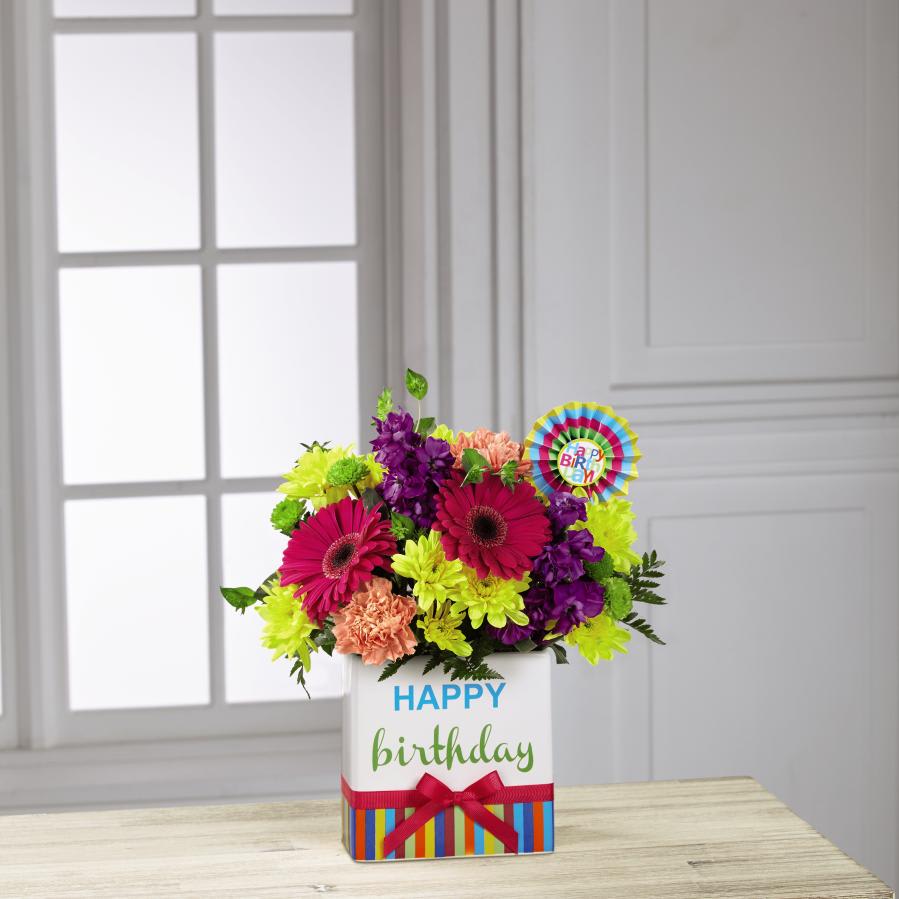 The FTDÂ¨ Birthday BrightsÂª Bouquet - The FTDÂ¨ Birthday BrightsÂª Bouquet is a true celebration of color and life to surprise and delight your special recipient on their big day! Hot pink gerbera daisies and orange roses take center stage surrounded by purple gilly flowers, yellow chrysanthemums, orange carnations, green button poms, bupleurum, and lush greens to create party perfect birthday display. Presented in a modern rectangular ceramic vase with colorful striping at the bottom, "Happy Birthday" lettering at the top, and a bright pink bow at the center, this unforgettable fresh flower arrangement is then accented with a striped happy birthday pick to create a fun and festive gift. GOOD bouquet includes 11 stems. Approx. 14"H x 11"W. BETTER bouquet includes 14 stems. Appro. 16"H x 12"W. BEST bouquet includes 18 stems. Approx. 17"H x 13"W. EXQUISITE bouquet includes 23 stems. Approx. 17"H x 14"W.