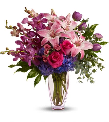 Pink lilies, roses, orchids, and blue hydrangeas in a clear vase