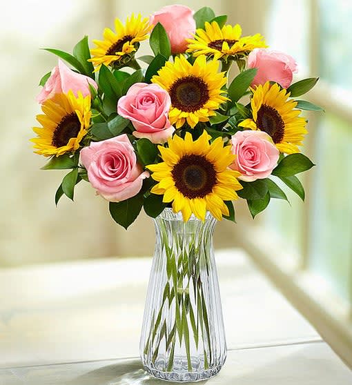 Pink roses and yellow sunflowers in a clear glass vase