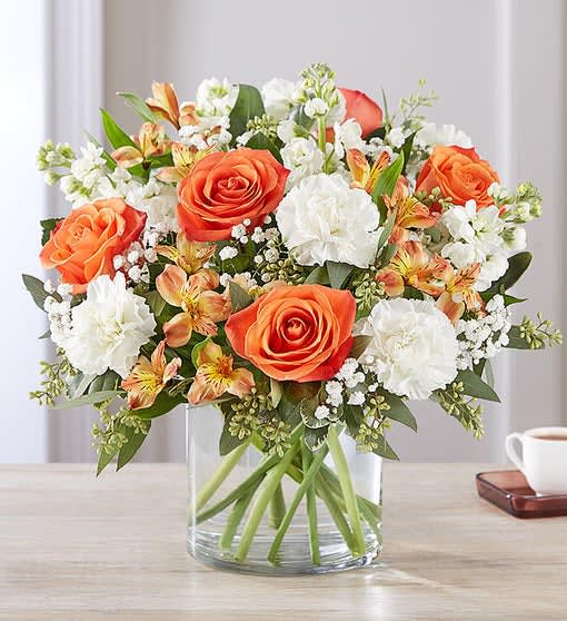 Orange roses and white flowers arranged in a clear glass vase