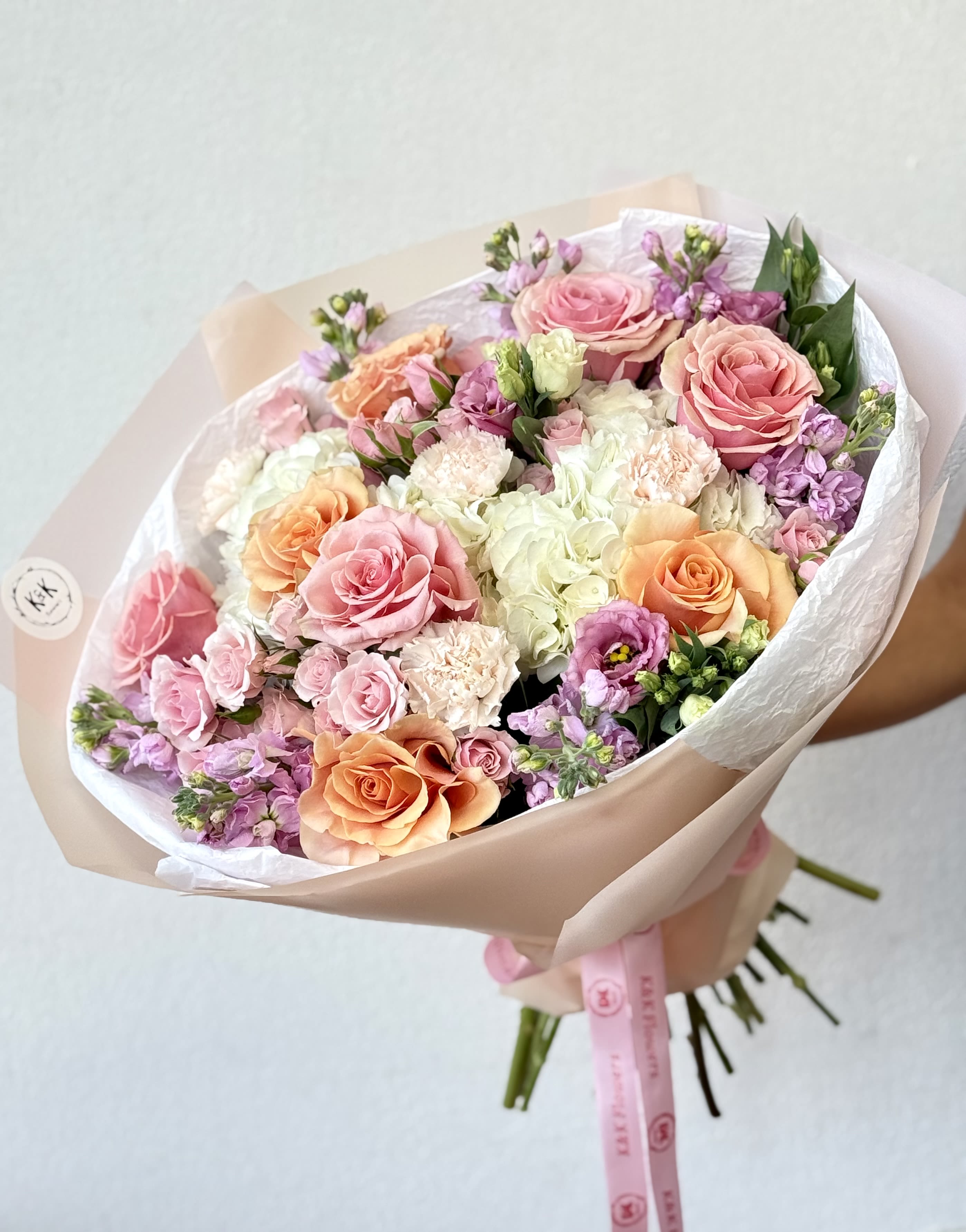 Hand-tied bouquet of pink, peach, and white roses with pastel filler flowers