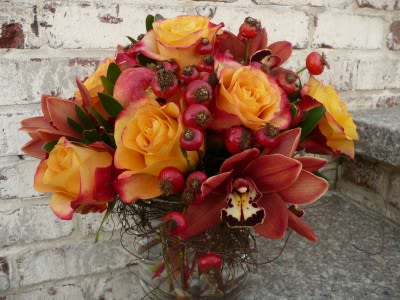 Low arrangement of yellow roses and rust orchids with red berries in a clear glass vase