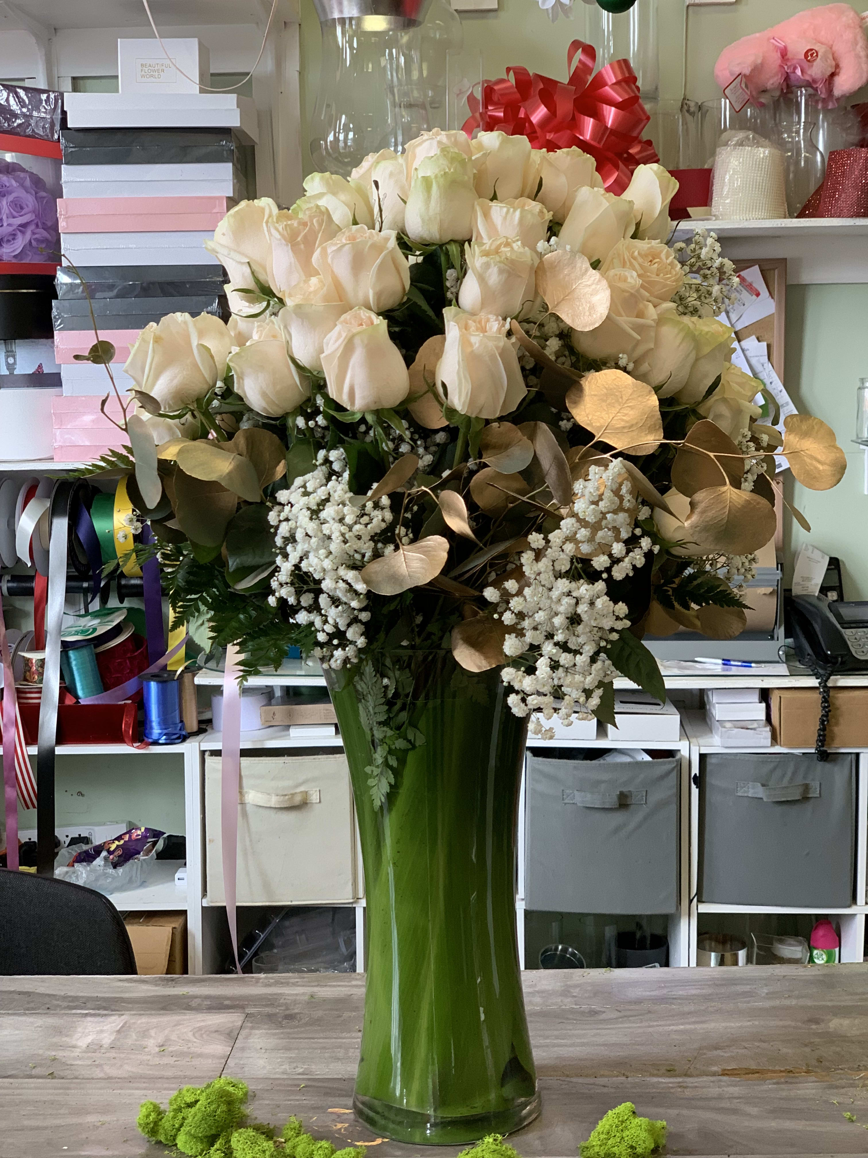 Cream roses in a tall green glass vase with gold-toned foliage