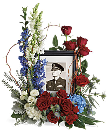 Floral tribute around a framed portrait with red roses and blue and white blooms