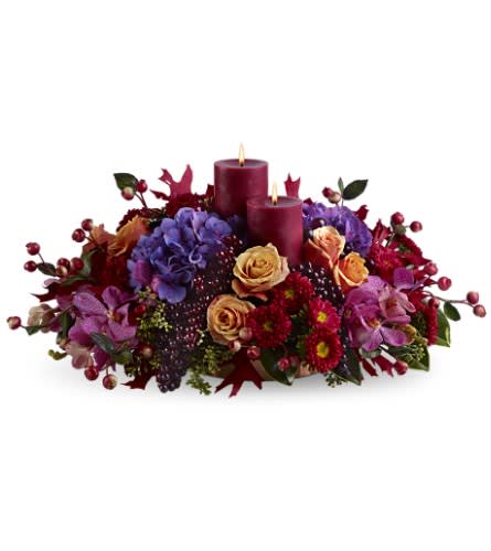 Merlot by Candlelight - The rich, exotic color of Merlot enjoyed by candlelight is captured in this spectacular centerpiece, created with orchids, roses and hydrangea in shades of purple, orange and red - mingled with grapes and berries, and artistically arranged around two burgundy pillar candles. Light up any event!