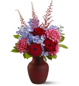 Sonoma Sunset - A sunset in wine country often appears as layers of deep red against a cool blue sky… and this enchanting mix of red roses, pink dahlias and more, set off to great effect by tall blue delphinium, recreates those vivid colors. A cranberry-red vase completes the pretty picture.