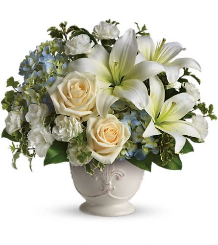 White lilies and cream roses in a decorative vase with blue hydrangeas