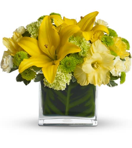 Yellow lilies and green-white flowers in a square glass vase