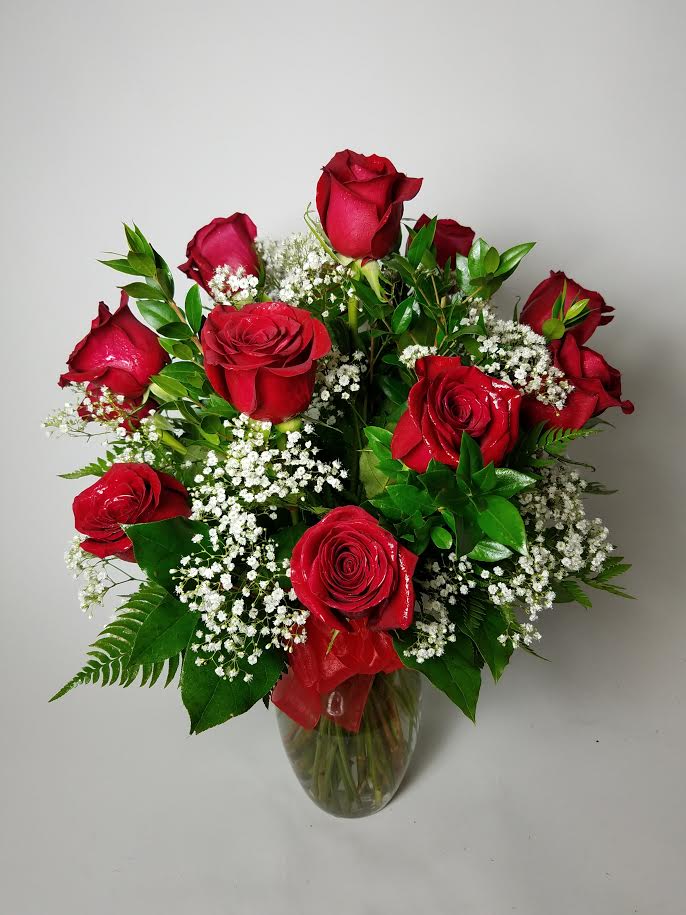 Red roses arranged in a clear glass vase with white filler flowers