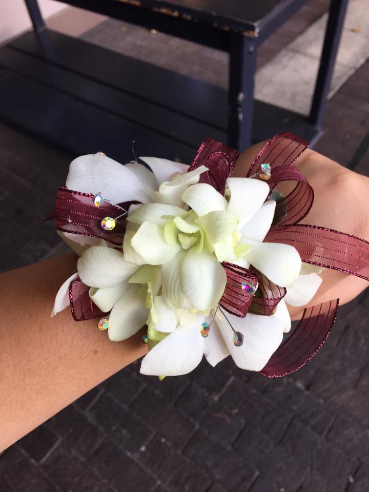 White orchid corsage with burgundy ribbon and rhinestone accents