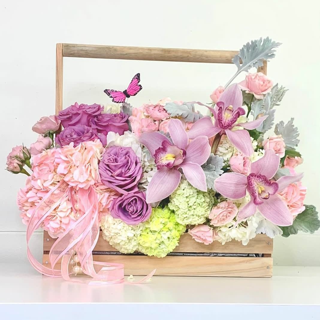 Pink and purple floral arrangement in a wooden box with orchids and roses