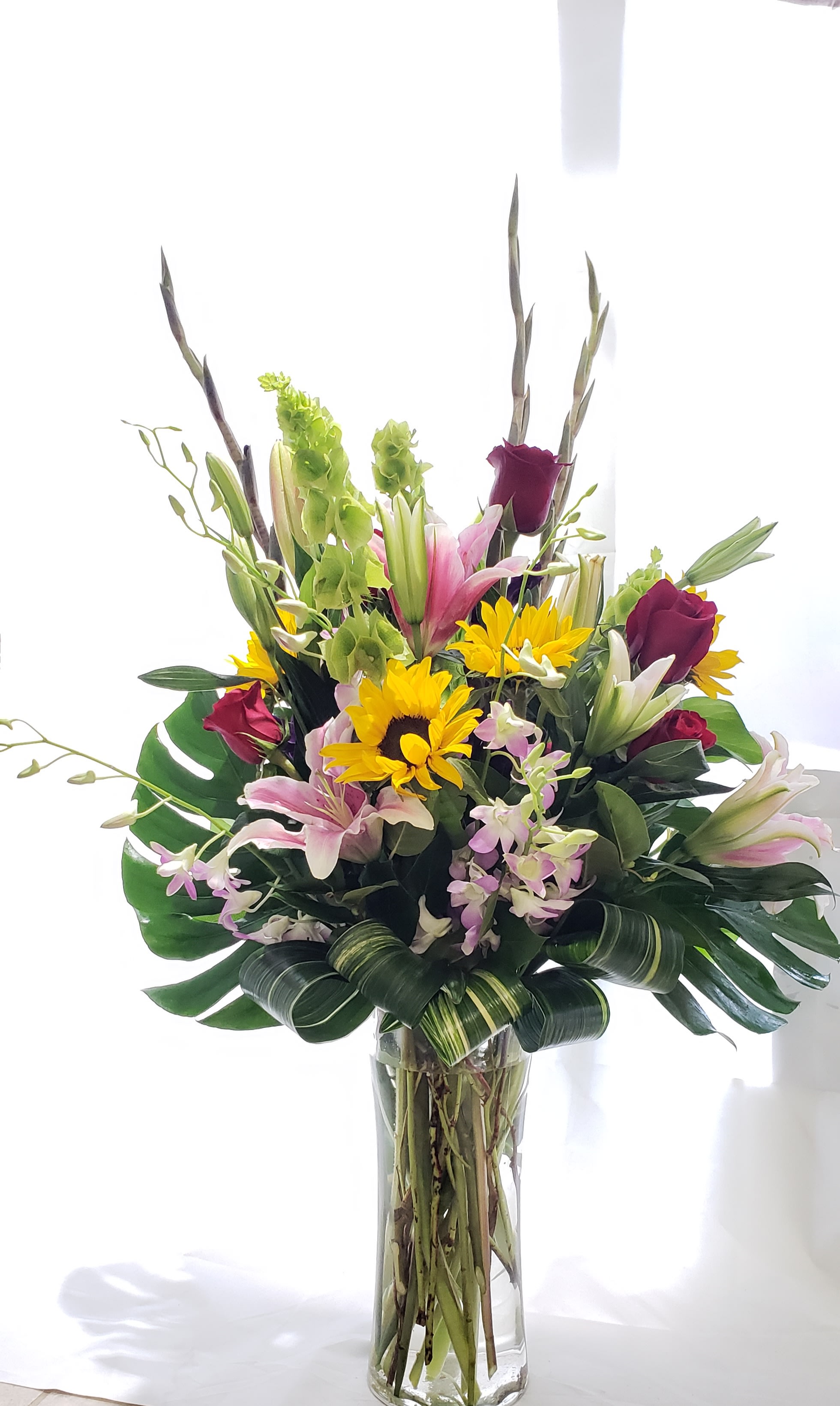 Tall mixed bouquet in a clear glass vase with lilies, roses, and sunflowers