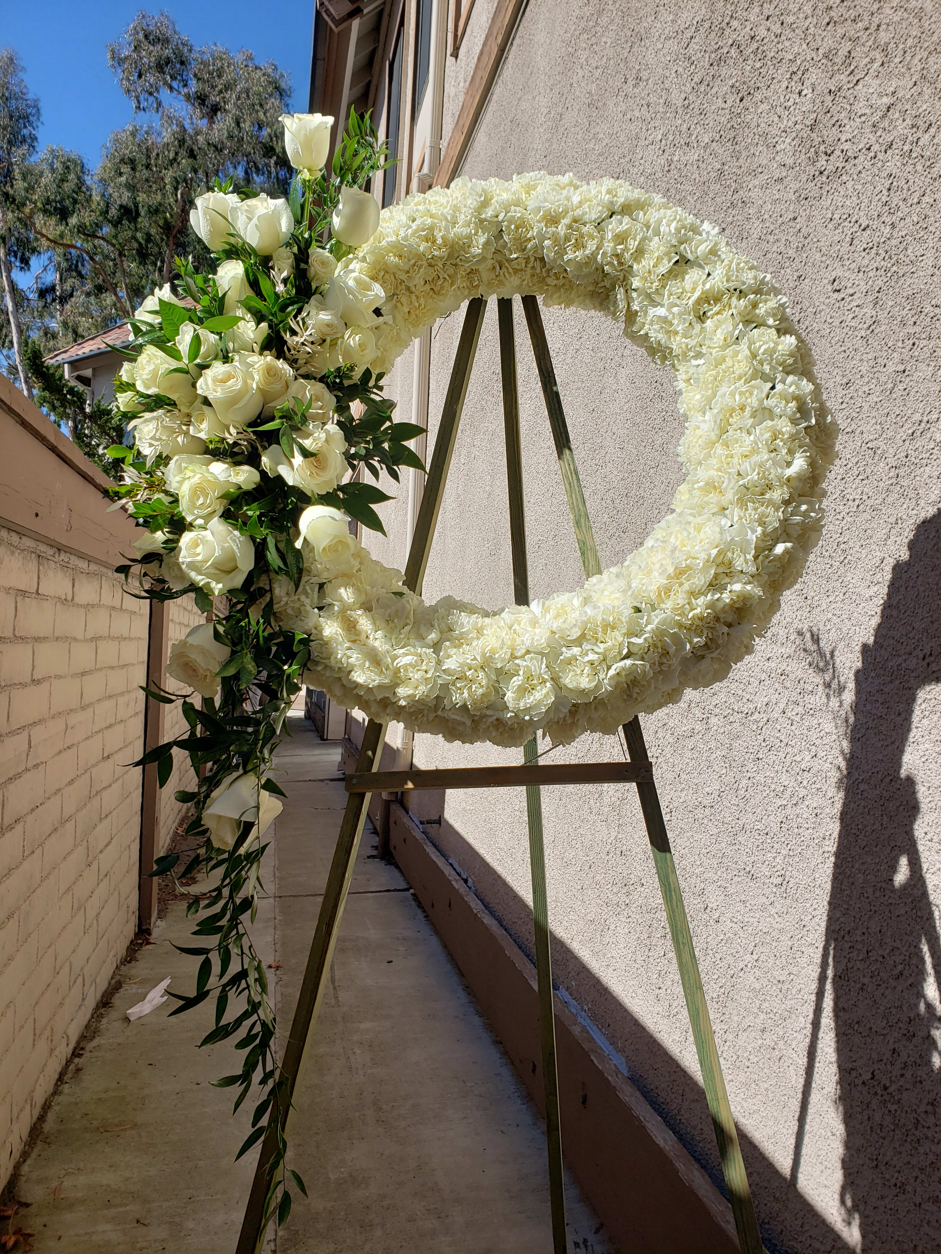 Large white floral wreath on an easel with roses and carnations