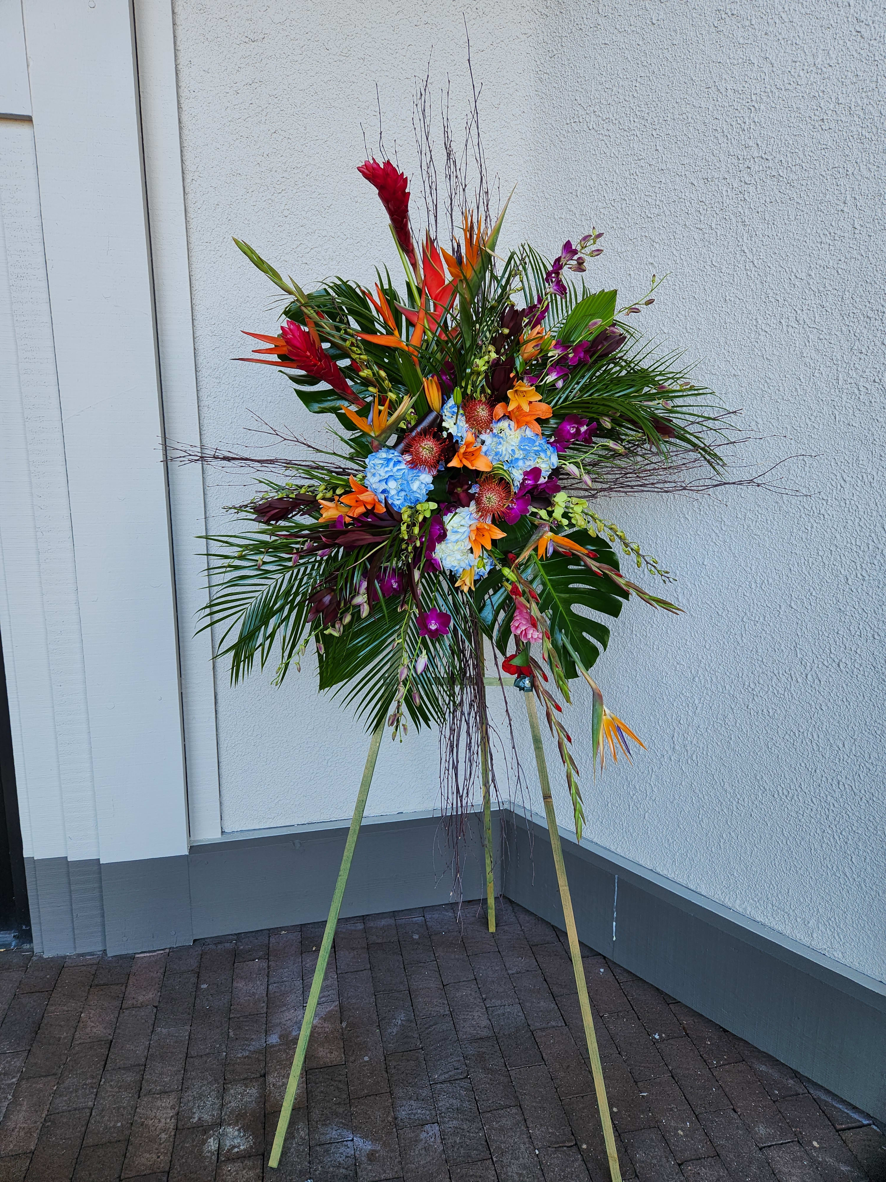 Tall tropical floral standing spray with bright mixed blooms on a tripod easel