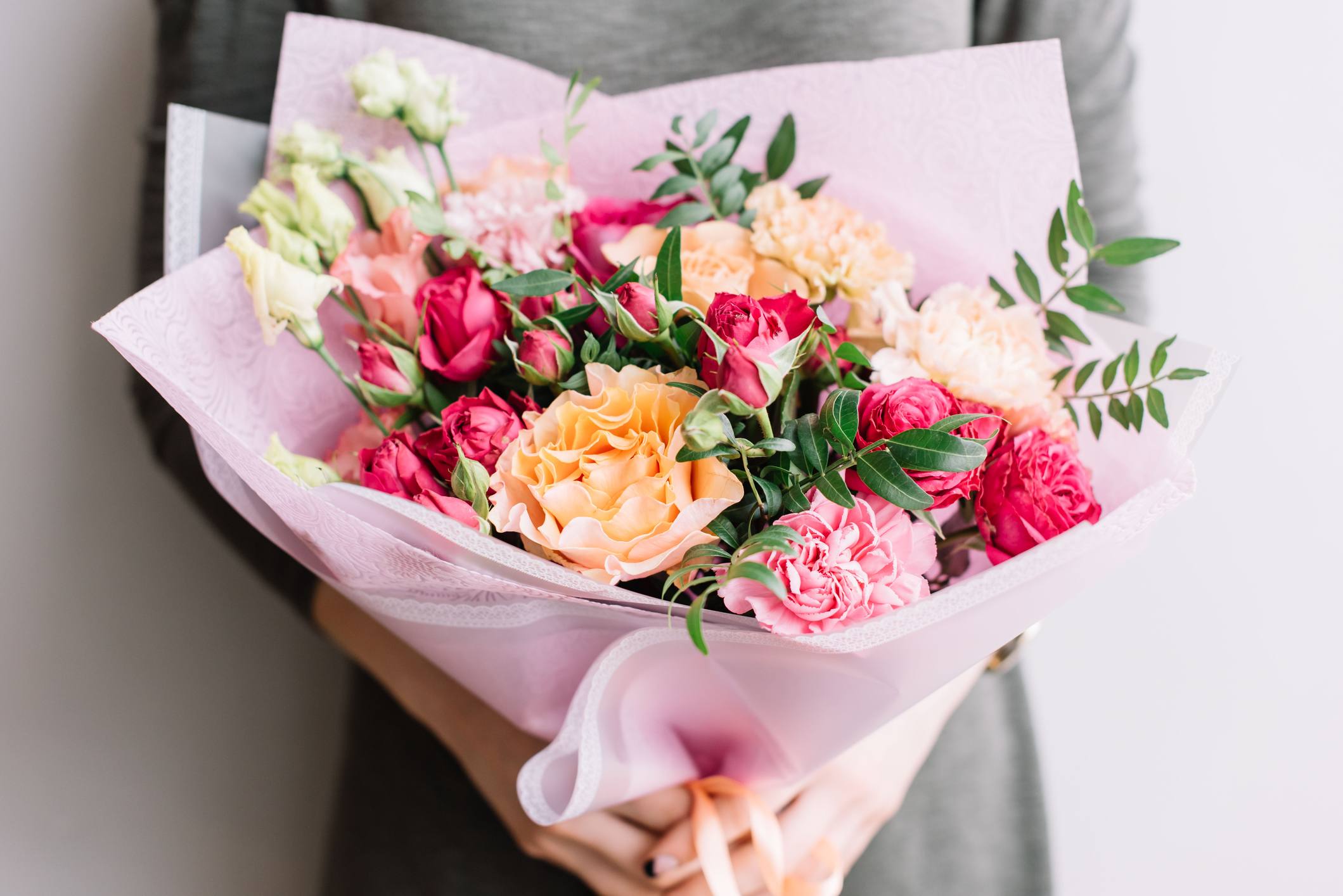 Bouquet of pink, peach, and white roses with carnations wrapped in pale pink paper