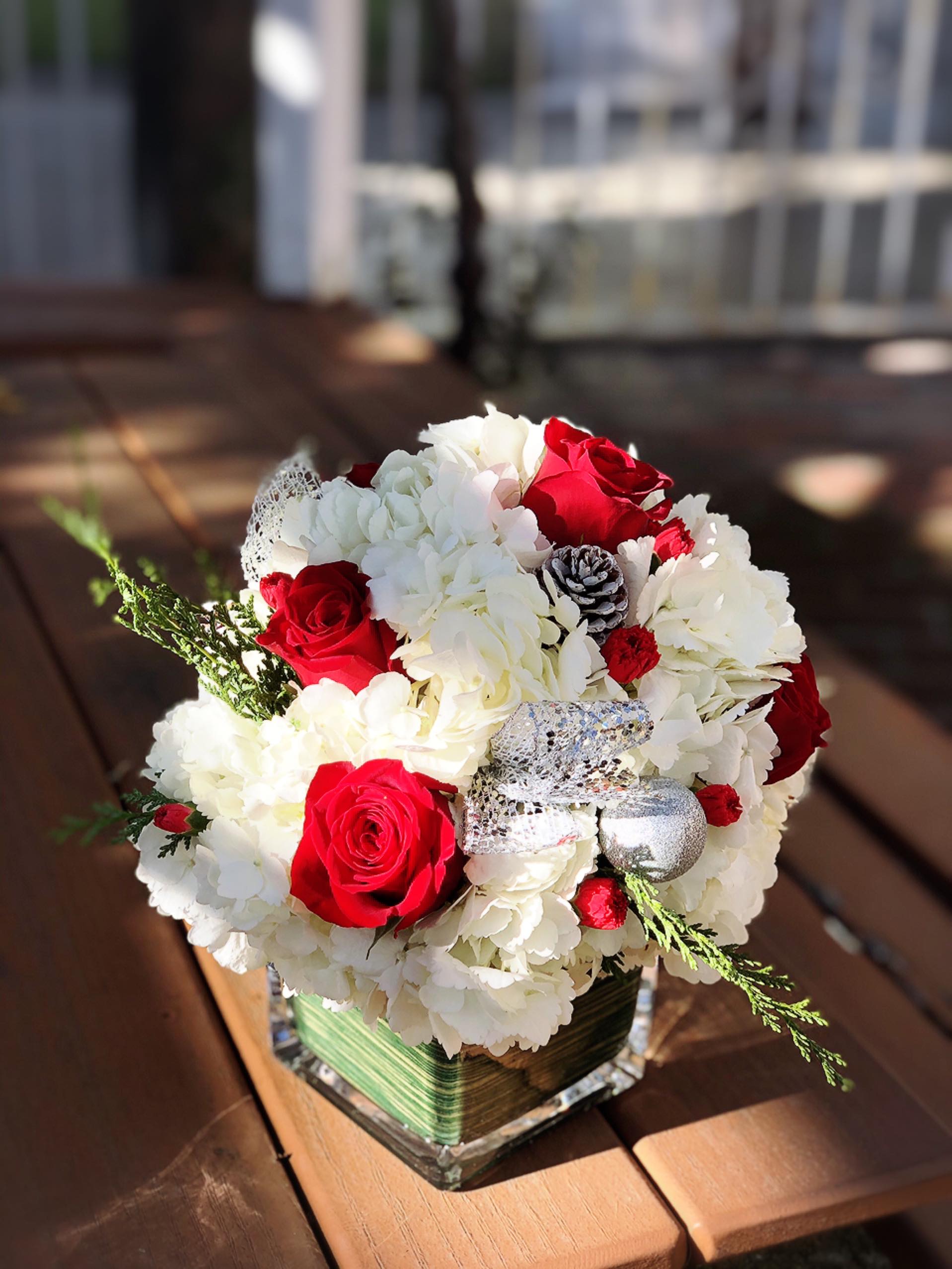 Joy Tonight - - 6 Red Roses - White Hydrangeas - 5 Red Carnations - Pine Cones - Christmas Greens - 4.75 inches glass cube vase