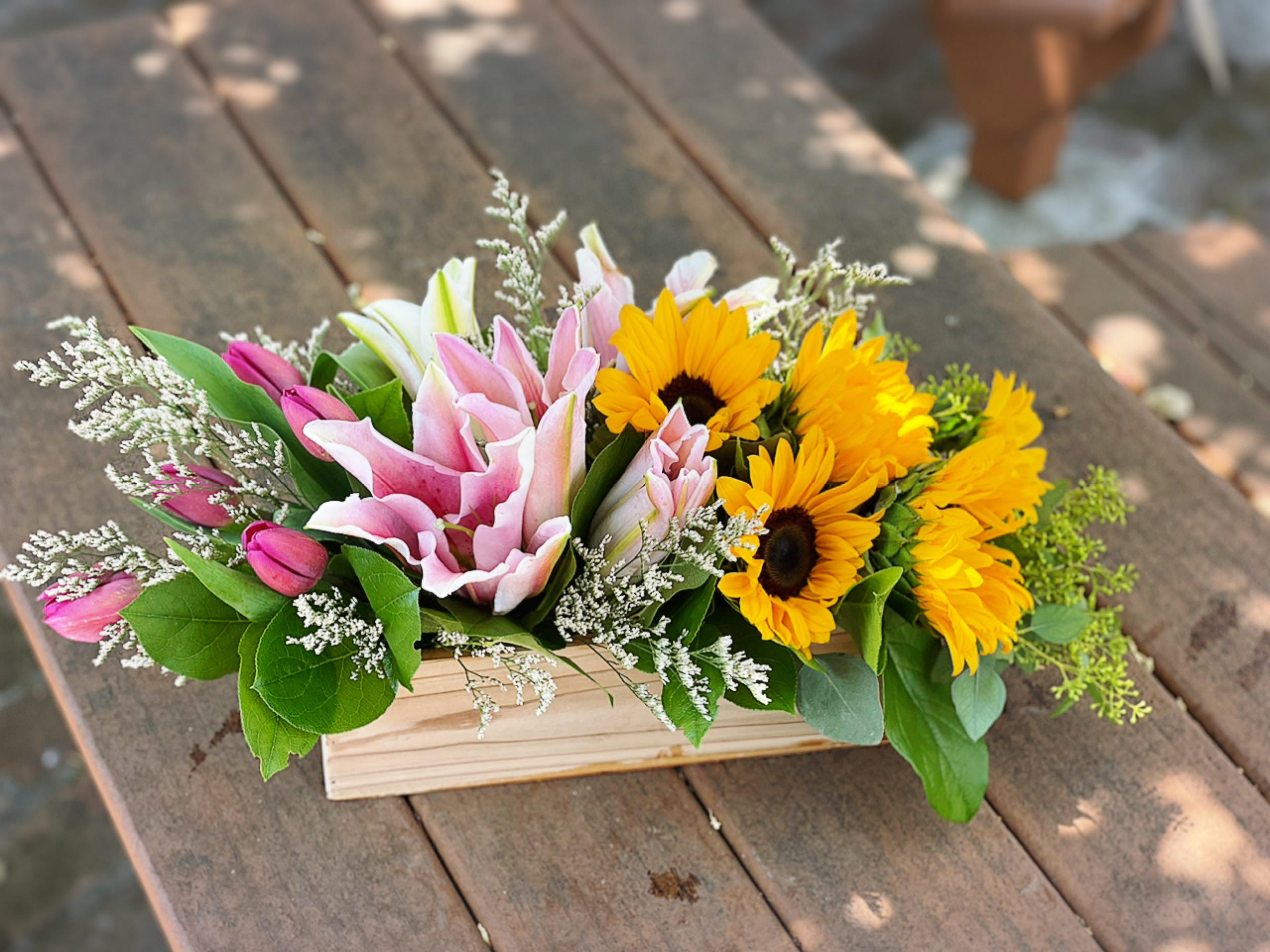 Pink lilies and yellow sunflowers in a wooden box