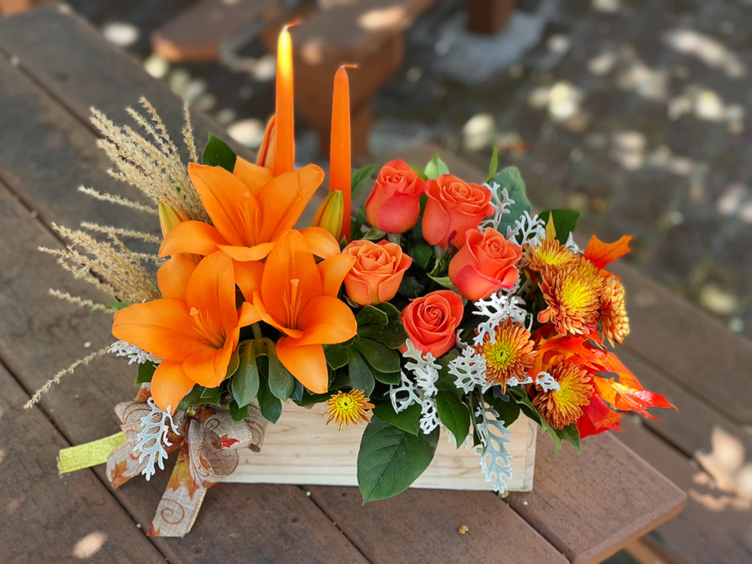 Thanksgiving Centerpiece (WoodBox) - - 3 Orange Lilies - 6 Orange Roses - 3 Fall Cushions - Dusty Millers - 2 Candles - 12 x 4 Inches Wood Box